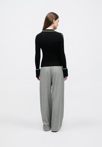 Must soonikkusega pikad varrukad must top valgete aksendiga detailidega; kombineeritud hallide laiade pükstega; sile tekstuur, keha järgnev lõige.