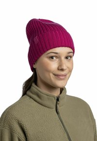 Magenta ribbed knit beanie with a slightly slouchy design. Features a small logo tag, worn by a person in a fleece jacket.