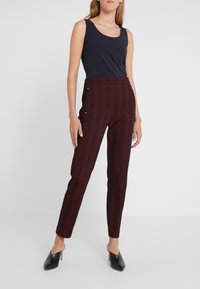 Černý top bez rukávů a kalhoty s vysokým pasem v burgundské kostce s bočními kapsami. Hladká tkanina, přiléhavý střih a špičaté černé podpatky.