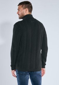 Dunkelgrauer gestrickter Pullover mit hohem Kragen, der ein geripptes Muster und strukturierte Details aufweist. Lange Ärmel und lässige Passform.