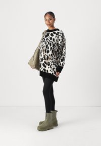 Oversized black and white leopard print sweater with ribbed cuffs, paired with black leggings and olive green chunky boots. Tote bag in hand.