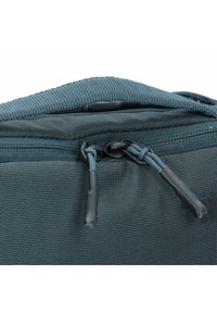 Sac zippé bleu foncé avec un tissu texturé. Présente des tirettes de zip noires et des coutures, ainsi qu'un accent de marque sur le côté.