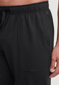 Zwarte joggingsbroeken gemaakt van zachte stof, met een elastische tailleband met een trekkoord, zijzakken en subtiele naaddetails.