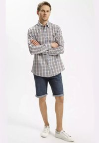 Biała, niebieska i brązowa w kratę koszula z długim rękawem, zestawiona z dżinsowymi szortami. Szare i białe sneakersy dopełniają całość.