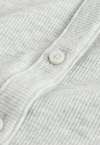 Gros plan sur un tissu rigide gris clair avec un bouton blanc cousu sur une patte de boutonnage texturée.