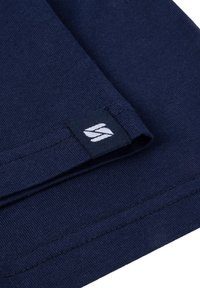 Navyblauwe katoenen stof met een gladde textuur, voorzien van een zwart label dat in de naad is genaaid, geperst met een wit logo.