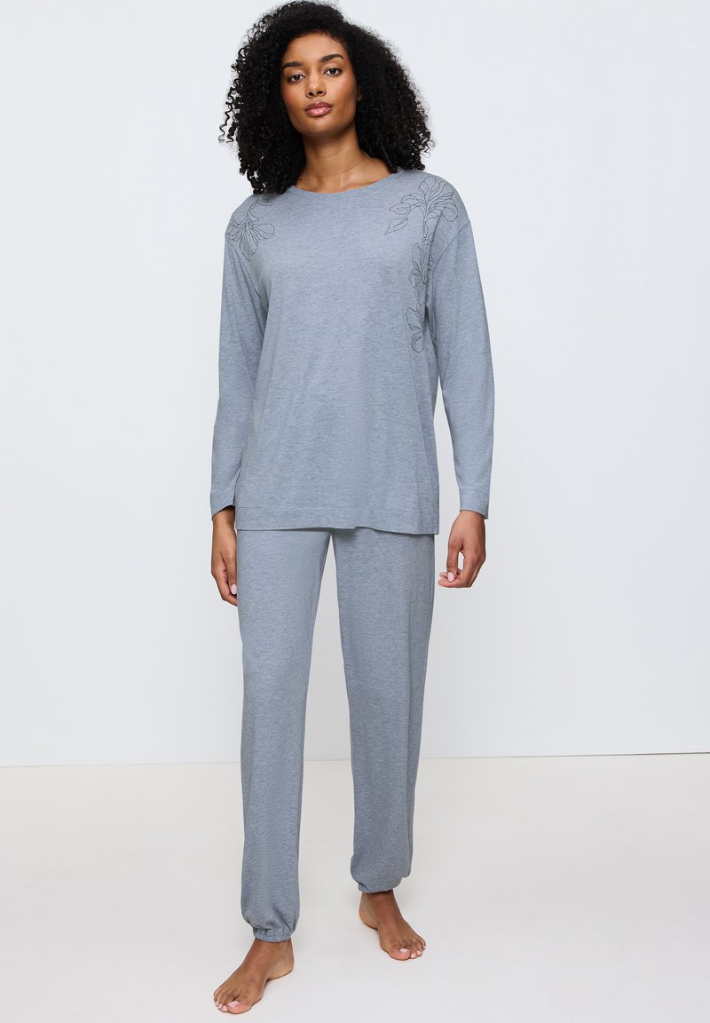 Set loungewear terang abu-abu yang terbuat dari kain lembut. Atasan lengan panjang dengan bordir bunga, potongan santai, dan manset elastis pada celana.