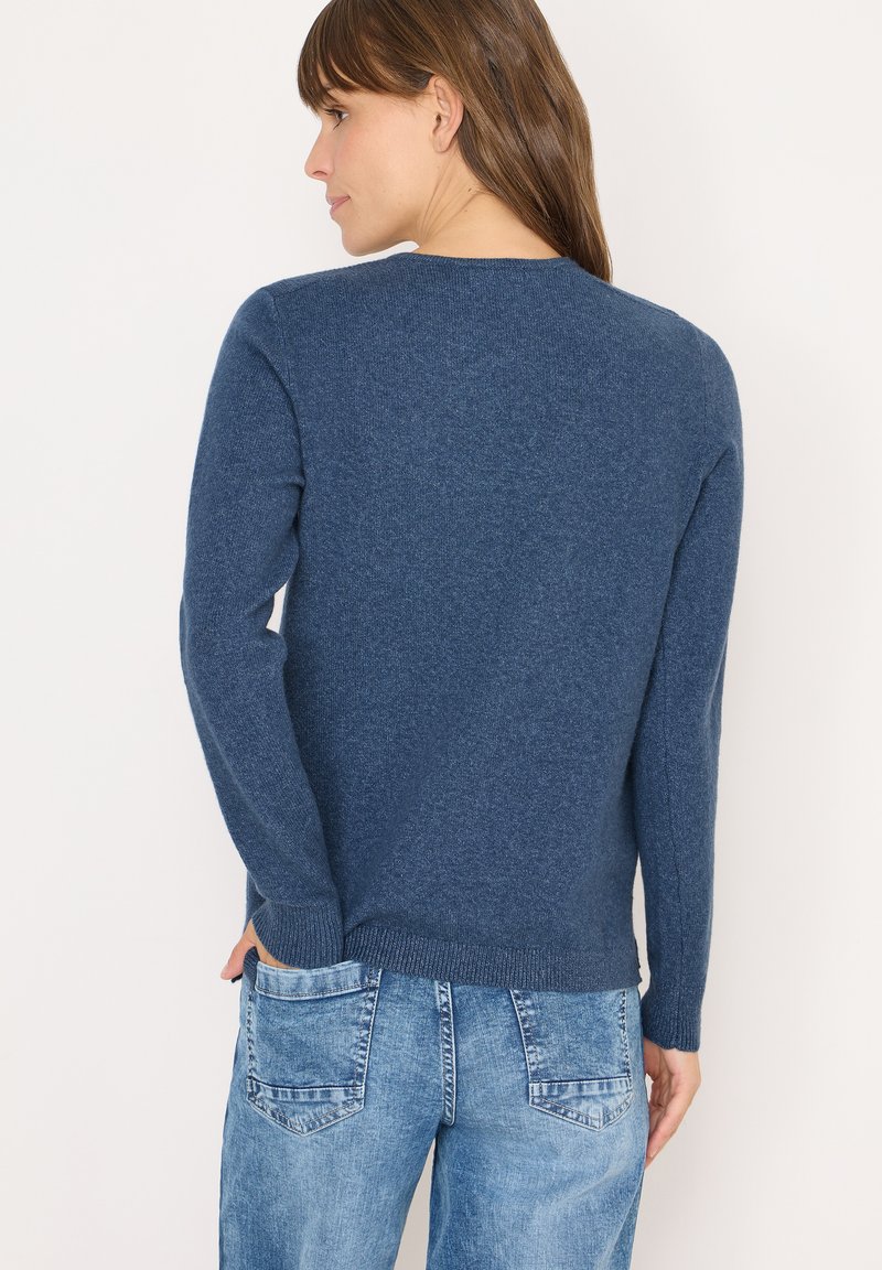 Maglione lavorato a maglia blu navy con maniche lunghe, scollo a barca e polsini a coste. Indossato con jeans in denim chiaro, che mettono in mostra un look casual.