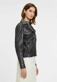 Schwarze Leder-Bikerjacke mit figurbetontem Schnitt, asymmetrischem Reißverschluss und gerippten Akzenten an den Ärmeln. Glatte Textur, Schulterklappen vorhanden.