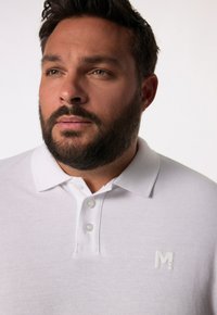 Bílá polokošile vyrobená z texturované látky, s límečkem, třemi knoflíky a malým logo značky na hrudi.