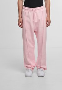 Pink sweatpants with a relaxed fit, elastic waistband, drawstring, and side piping detail, paired with white sneakers.
