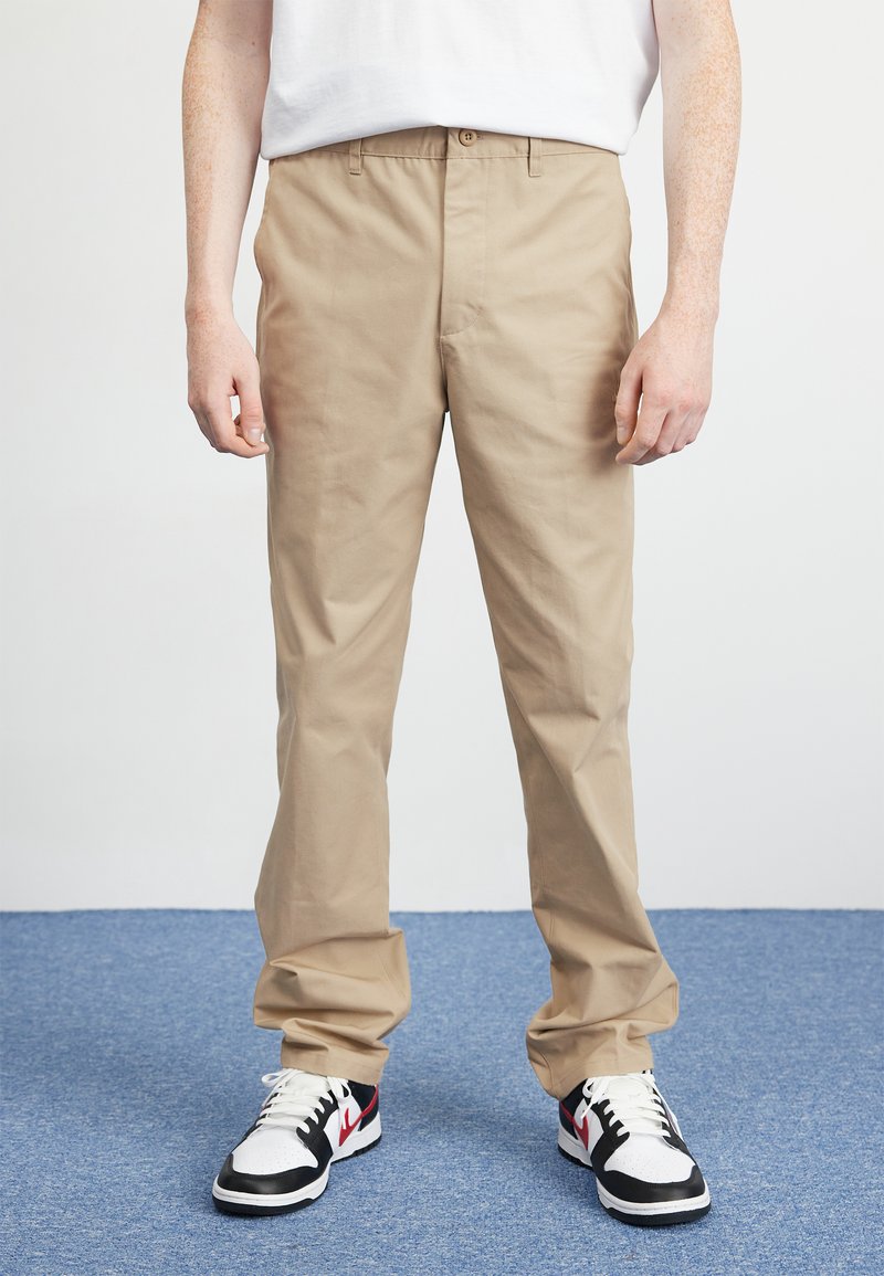 Khaki trousers with a straight leg design, made of cotton. Features a button closure and two front pockets, paired with black and white sneakers.