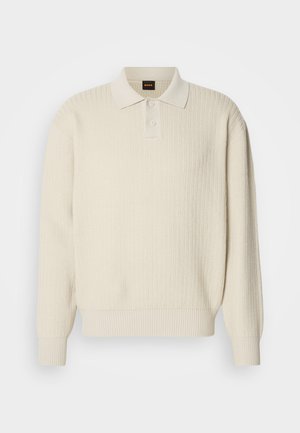 Pleteni pulover boje kreme s rebrastom teksturom, s preklopnim ovratnikom i dva dugmeta na vratu. Dugi rukavi s rebrastim manžetama i rubom.