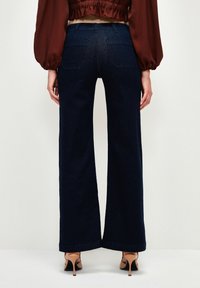Jeans de mezclilla de pierna ancha en un oscuro tono azul, con una textura suave, diseño de cinco bolsillos y costuras en contraste. Presentan una cintura alta y un dobladillo ajustado.