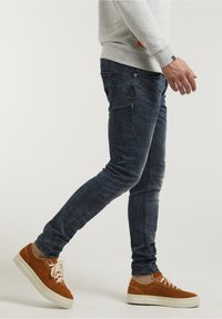 Mörkblå jeans med slim fit, med en blekt textur. Tillsammans med bruna mockasneakers och en ljusgrå sweatshirt.