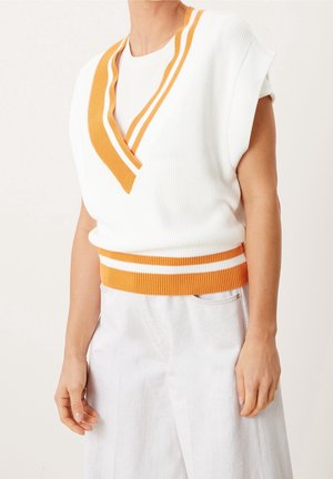 Person iført hvid strikket ærmeløs sweatervest med orange stribet V-hals og taljebånd, kombineret med lyse bukser.