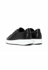 Sneakers in pelle nera con finitura liscia, punta tonda, suola in gomma bianca e lacci a contrasto. Nessun marchio o logo visibile.