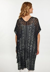 Kimono crochetat negru cu un model deschis, cu mâneci scurte și un design fluid. Are ciucuri pe laterale și un guler rotund.