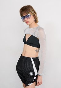 Black bikini top with triangular cut, silver mesh long-sleeve top, and black athletic shorts with white stripe and logo detail. Blue sunglasses.