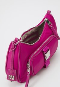 Borsa a mano in nylon rosa con hardware argentato, dotata di due scomparti con cerniera e un dettaglio a fibbia sulla patta frontale. Inclusa tracolla regolabile.