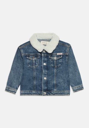 Veste en denim bleu avec col sherpa blanc, fermeture à boutons, deux poches poitrine et étiquette Calvin Klein sur la poche gauche.