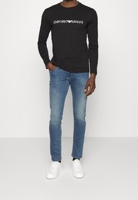 Svart långärmad t-shirt med vit "Emporio Armani"-logotyp, i kombination med ljusblå jeans och vita sneakers. Avslappnad outfit.