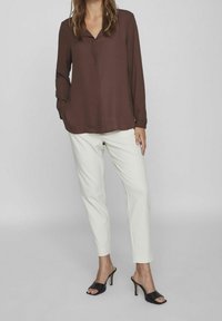 Brun långärmad blus med V-ringning, matchad med vita avsmalnande byxor och svarta öppna klacksandaler. Släta tyger och skräddarsydd passform.