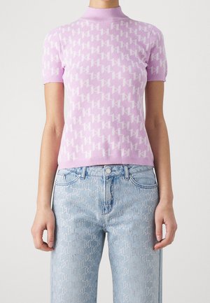 Personne portant un top en maille lilas à manches courtes avec un motif géométrique blanc et un jean bleu clair avec un motif subtil assorti.