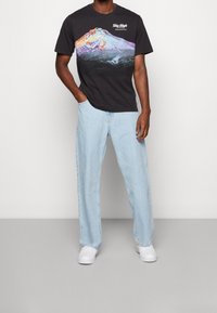 Svart t-shirt med bergsgrafik och texten "Sky High", parat med ljusblå vida jeans och vita sneakers. Avslappnad outfit.