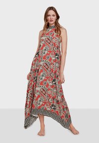 Vestido maxi con cuello halter, con base en color coral, patrones florales en negro y crema, y un dobladillo asimétrico con un borde decorativo.