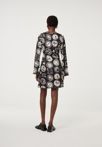 Schwarz langärmliges Kleid mit einem weißen Druckmuster mit kreisförmigen Designs. Glatter Stoff, A-Linie Form und Knopfdetails auf der Rückseite.