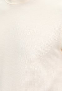 Κρεμ χρωματισμένο υφασμάτινο πλεκτό με απαλή κεντημένη λογότυπο στην περιοχή του στήθους.