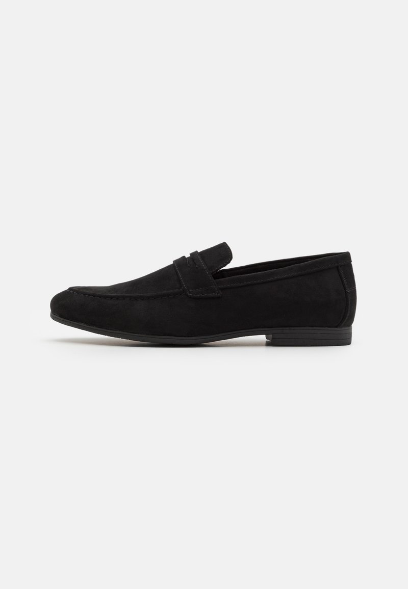 Mocassins en daim noir avec un bout arrondi, dotés d'une lanière frontale et d'une semelle en caoutchouc texturée basse. Surface lisse, design simple.