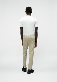 Pantalons beiges à coupe droite avec deux poches arrière, portés avec un t-shirt blanc uni et des chaussures noires, vus de dos.