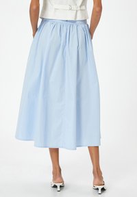 Falda azul claro hasta la rodilla con cintura fruncida y textura suave, combinada con sandalias de tacón blancas.