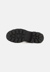 Suela de bota negra de goma con un patrón de banda de rodadura agresivo y profundo, y una sección central lisa. Construcción robusta para tracción y durabilidad.