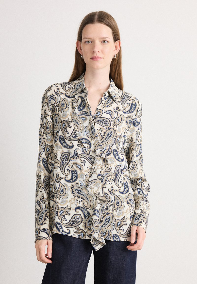 Langærmet bluse i creme med blå og gylden paisley mønster. Har en knaplukning foran og blødt stof med en afslappet pasform.