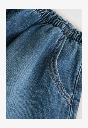 Close-up van denim stof met een gegatherde tailleband en contrasterende stiksels, met een zijzak en de textuur van het materiaal.