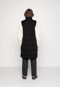 Czarna pikowana kamizelka z wysokim kołnierzem, z poziomymi przeszyciami. Widok od tyłu ukazuje długi, lekko zwężający się fason.