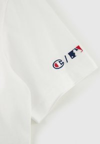 Witte katoenen T-shirt met korte mouwen, voorzien van een geborduurd rood en blauw Champion-logo en MLB-logo op de linker mouw.