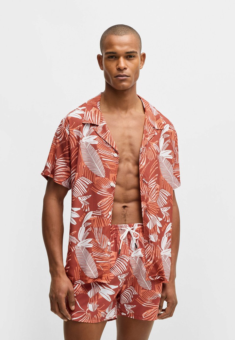 Red and white floral-patterned short-sleeve shirt and matching shorts made of lightweight fabric, featuring a relaxed fit and drawstring waist.
