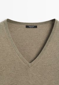 Olivgrüner V-Ausschnitt-Pullover aus weichem Stoff. Mit einem gerippten Ausschnitt und glatter Textur. Etikett sichtbar im Kragen.