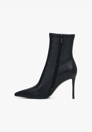 Czarny botek za kostkę wykonany z gładkiego syntetycznego materiału, z zaostrzonym noskiem i wysokim szpilkowym obcasem, zapinany na boczny zamek.