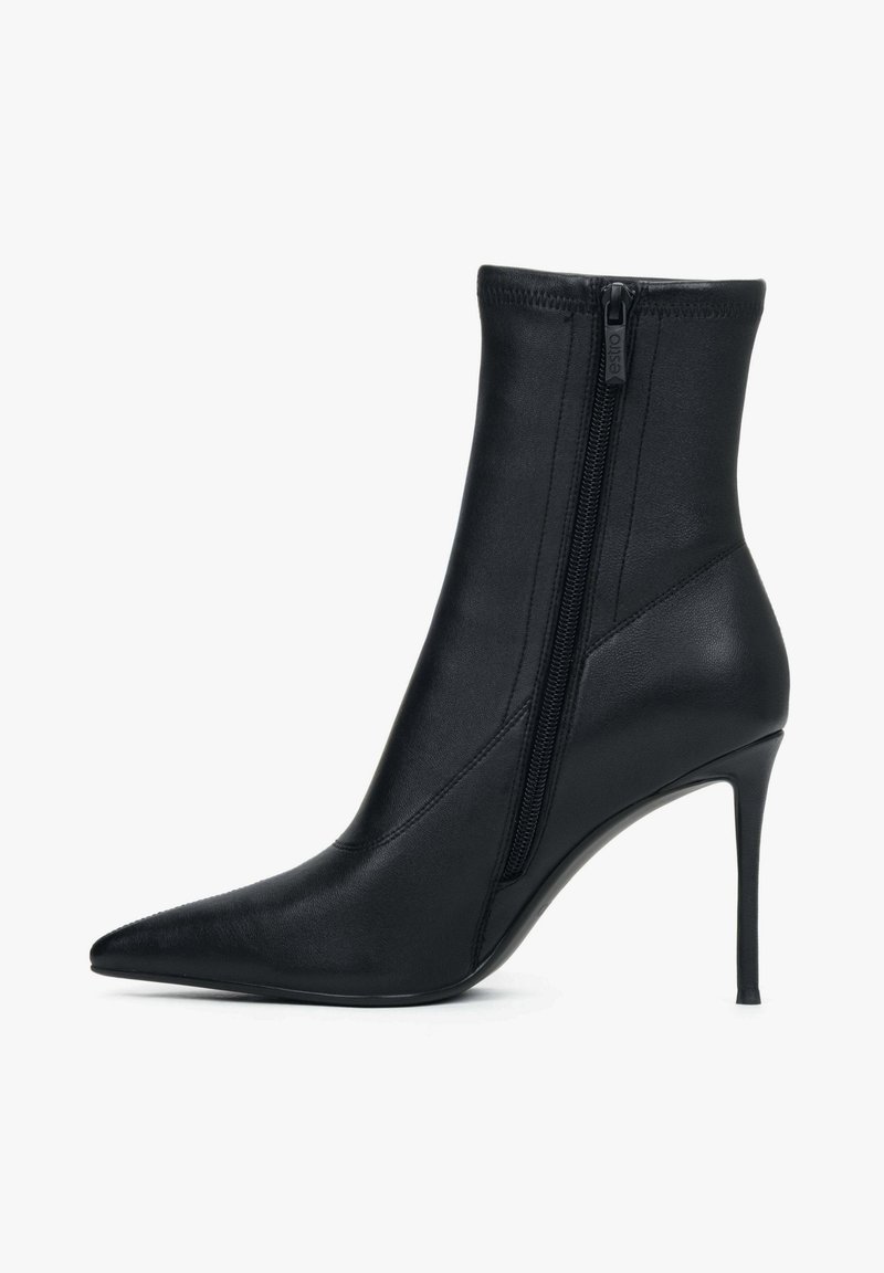Zwarte enkellaars gemaakt van glad synthetisch materiaal, met een puntige neus en een hoge naaldhak, voorzien van een zijrits als sluiting.