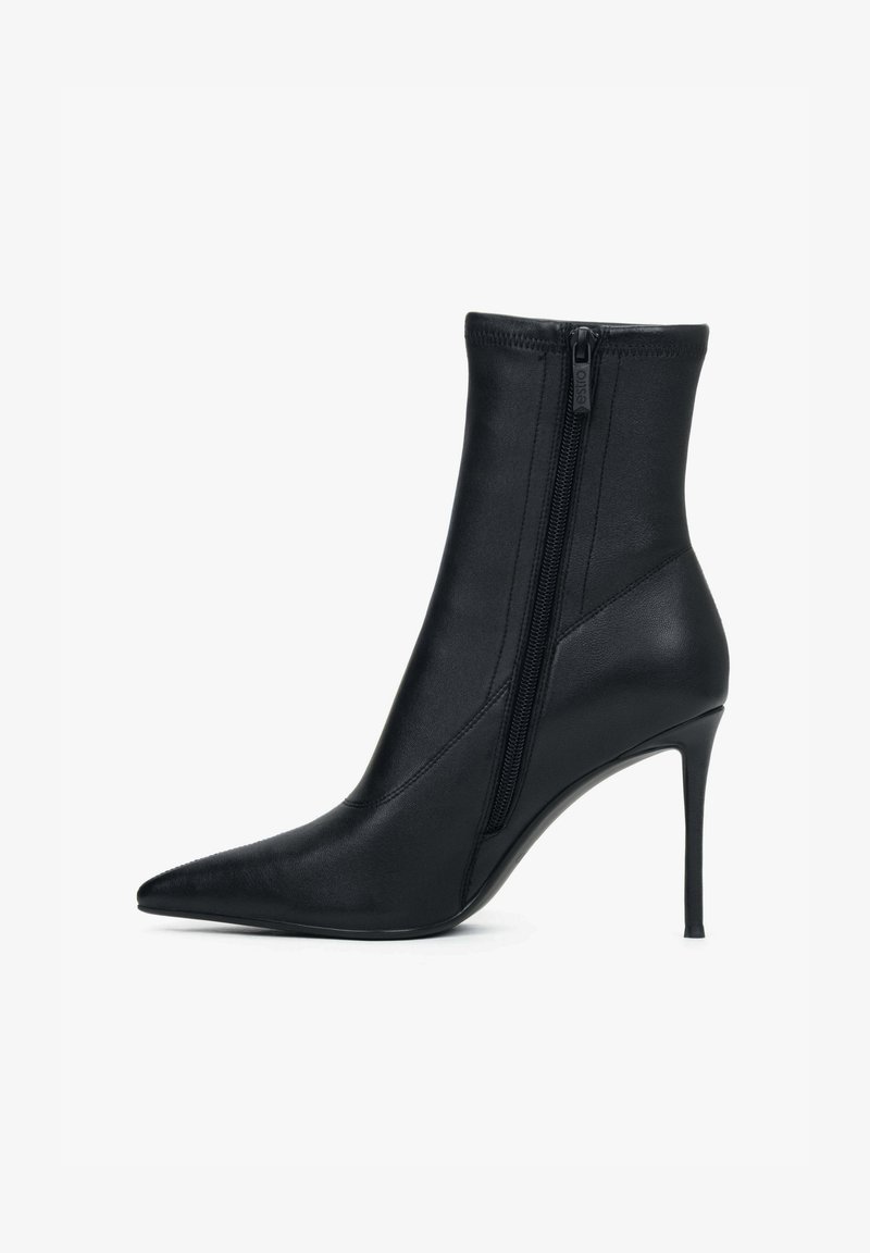 Zwarte enkellaars gemaakt van glad synthetisch materiaal, met een puntige neus en een hoge naaldhak, voorzien van een zijrits als sluiting.