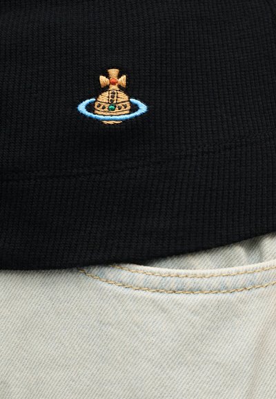 Έμβλημα σφαίρας σε χρυσό και τιρκουάζ με μπλε δαχτυλίδι κεντημένο σε μαύρο υφασμάτινο ύφασμα πάνω από ραφή φωτεινού τζιν.