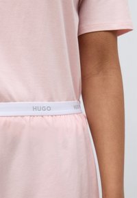 Ροζ φόρεμα με στρογγυλή λαιμόκοψη και κοντά μανίκια, με λευκή ελαστική ζώνη στη μέση με το λογότυπο «HUGO». Κατασκευασμένο από μαλακό ύφασμα, προσφέρει άνετη εφαρμογή.