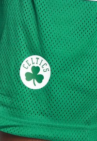 Tessuto verde di una maglia sportiva con piccoli fori di ventilazione e un logo circolare bianco dei Celtics che presenta un trifoglio verde e testo verde.
