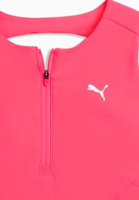 Combinaison de sport rose avec une fermeture éclair à l'avant, fabriquée à partir d'un matériau lisse. Affiche un logo Puma blanc sur la poitrine.