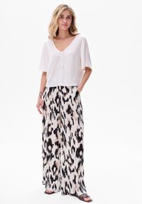 Haut blanc à col en V avec des manches courtes et larges, associé à un pantalon fluide à jambes larges dans un motif animal noir et crème.